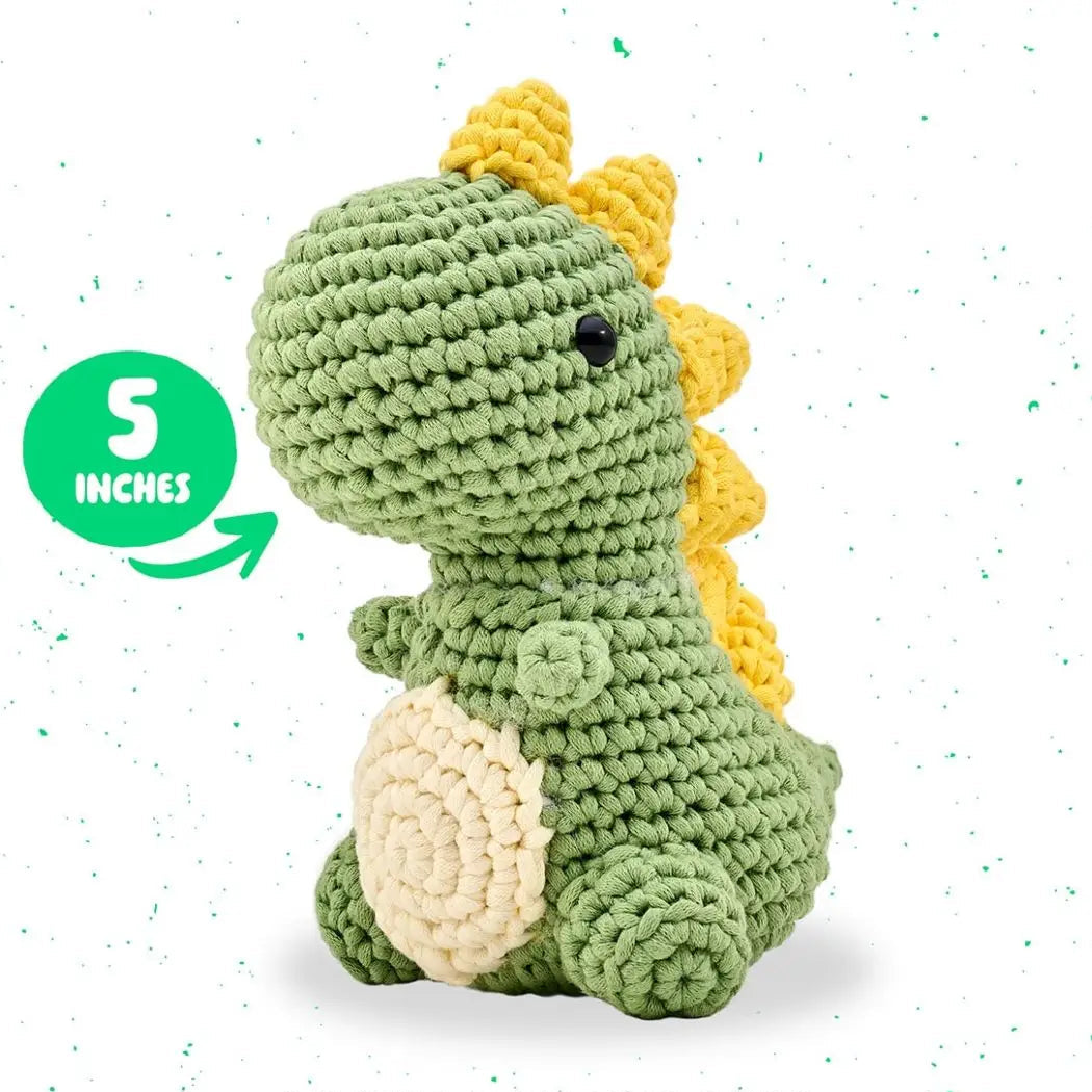 Crocheted dinosaur toy with green body, yellow spikes, and beige belly on a white background.