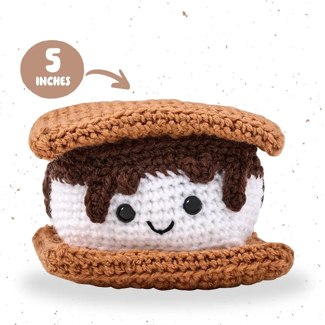Crocheted toy resembling a s'more with a smiling face on a white background