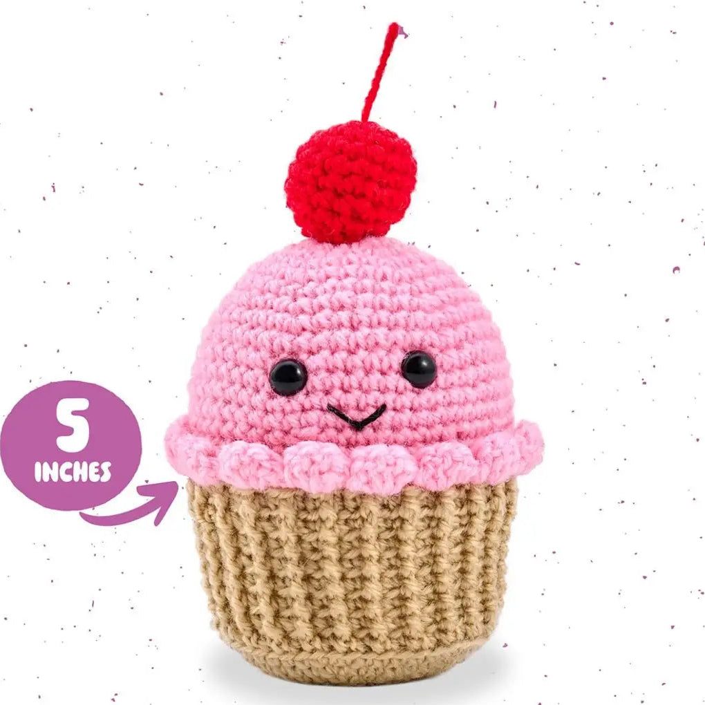 Crocheted cupcake toy with pink icing, brown base, and red cherry on top against a white background.