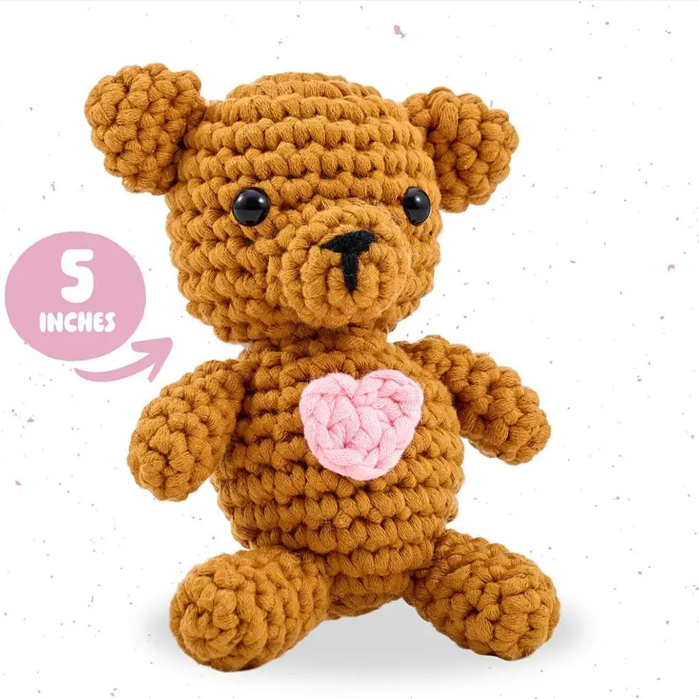 Crocheted bear toy with a pink heart on a white background